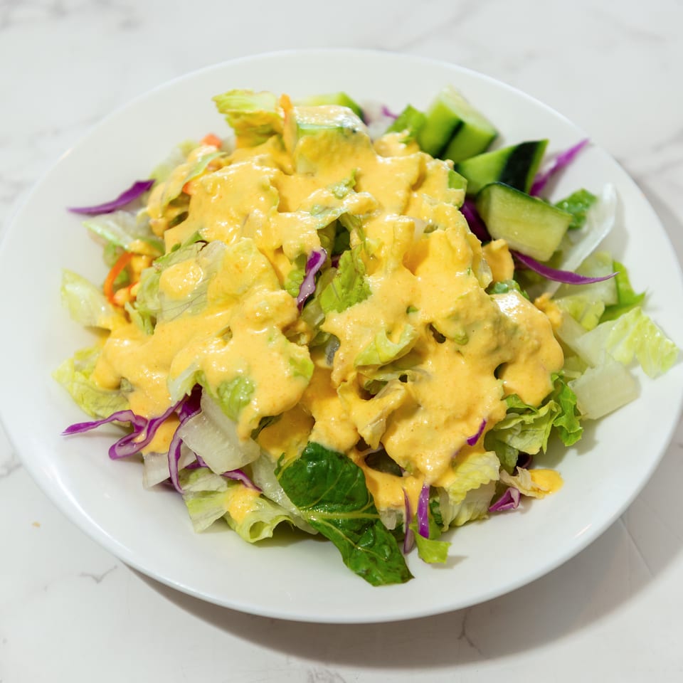 Mixed green salad with cucumber, shredded purple cabbage, and carrots topped with creamy orange dressing on a white plate.