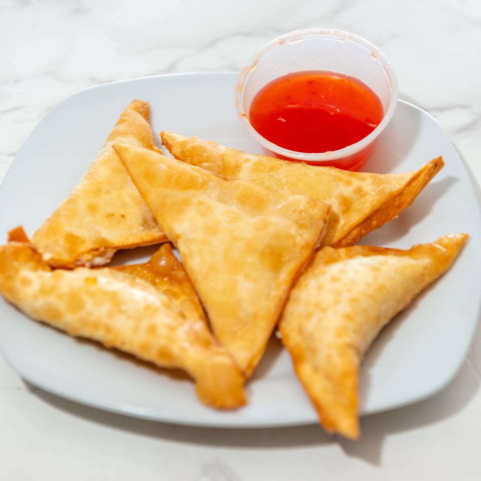 Golden fried triangular pastries arranged on a plate with a cup of red dipping sauce.