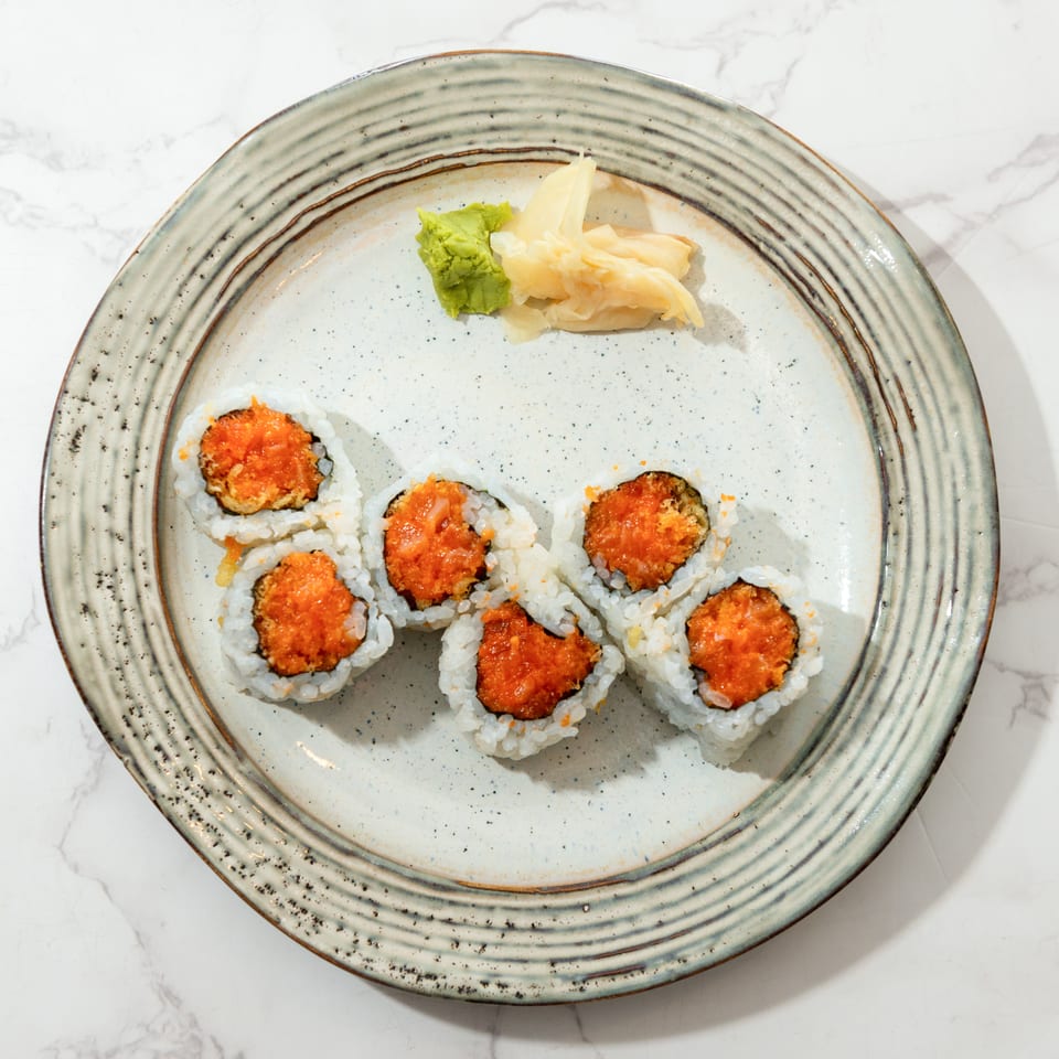 Plate of sushi rolls topped with orange sauce, accompanied by wasabi and pickled ginger on a marble table.