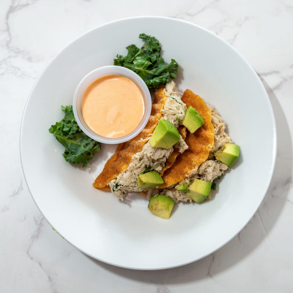 Crispy crab-topped tortillas with avocado, kale garnish, and creamy orange dipping sauce on a white plate.