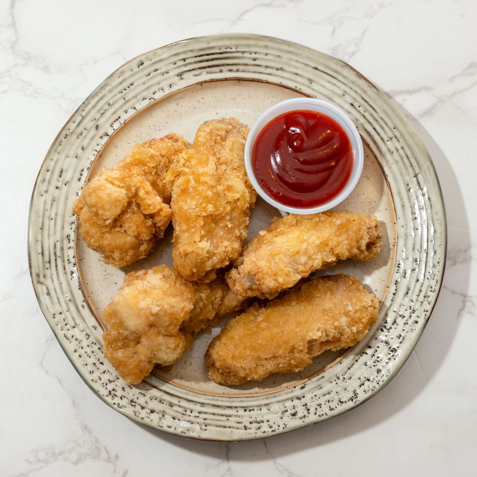 Golden fried chicken pieces arranged on a decorative plate with a small bowl of ketchup.