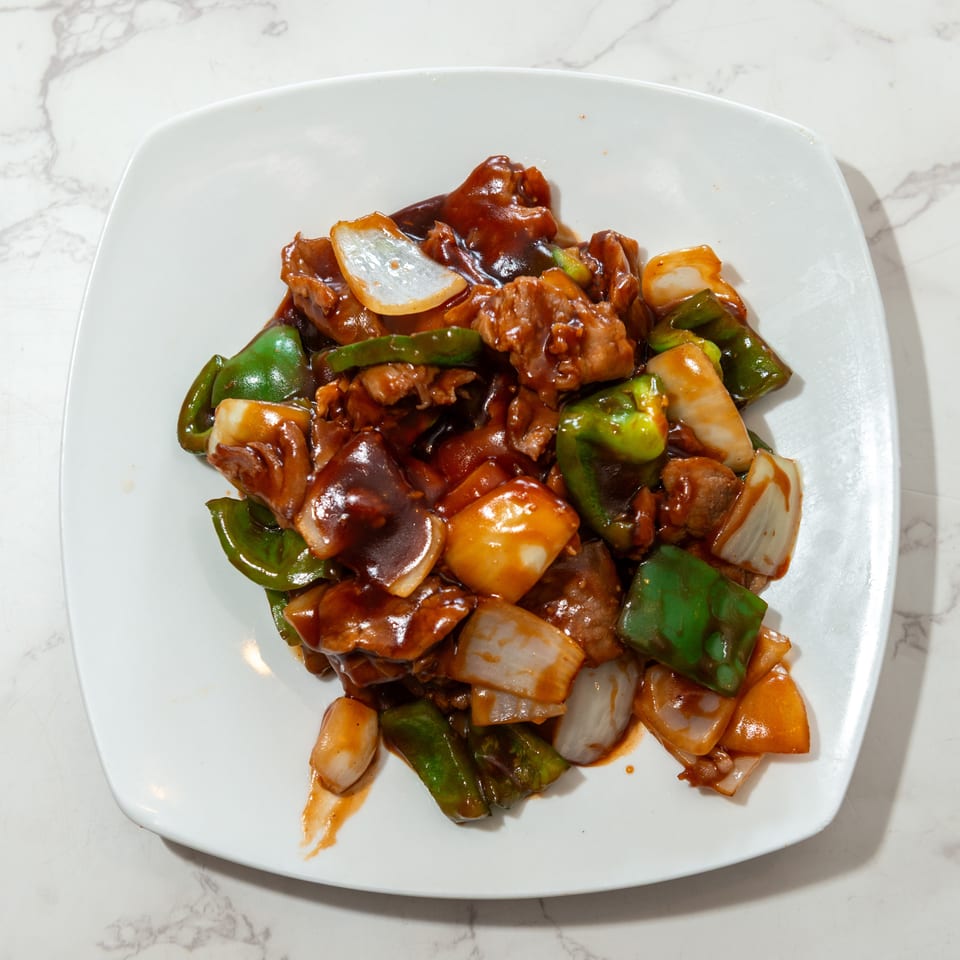 Stir-fried meat with green peppers, onions, and vegetables in glossy brown sauce on a white plate.